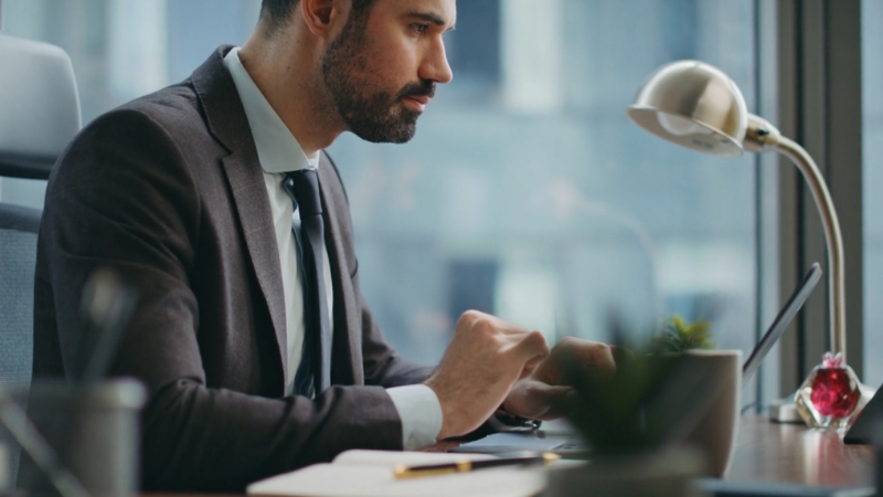 Poslovni čovek sedi za stolom i radi na laptopu