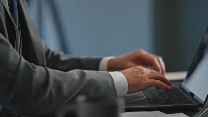 Muškarac u odelu kuca na laptopu za stolom